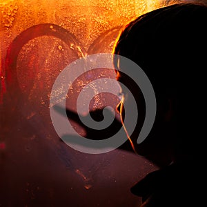 A boy draws a heart on a frosty window