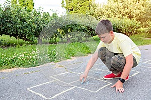 The boy draws on the pavement with chalk in the park. Games in the park