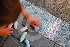 The boy draws a rainbow colored chalk on the pavement