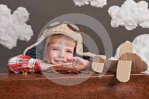 Boy dressed as an airplane pilot sit between the clouds with old suitcase and playing with handmade plane