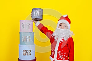A boy dressed in the clothes of Sanat Claus picked up the topmost gift box with the inscription New Year 2022