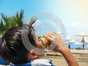 Boy drinking a drink on the beach on a hot summer day