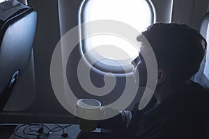 A boy drinking from paper cup sitting near airplane window during air flight. Food served on board