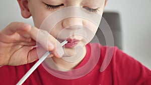 boy drinks juice from a straw, close up. Boy quenches his thirst and drinks soda from glass through straw.