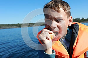 Boy eating apple in life jacket on boat