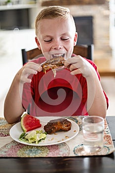 Boy eating a delicious plate of Barbecue ribs, watermelon and salad