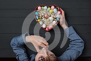 Boy eating Easter egg. Heart shaped box with colorful eggs in hand. Top view