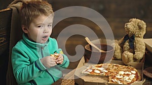 Boy eating pizza on a wooden background. Tasty pizza. Little boy having a slice of pizza. Hungry child taking a bite