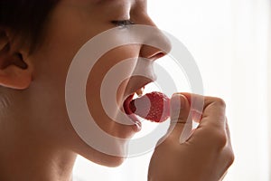 Boy eating a very tasty strawberry on a light background. Close up