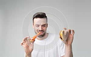 Boy eats an carrot and hamburger. Man makes the choice between fast and healthy food. Tasty or useful The dilemma