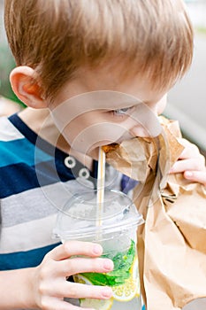 The boy eats a pie and drinks lemonade on the street. Street food. Snack for the child