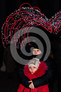 A boy embraces a girl against the background of the new year`s illumination of the arch of hearts