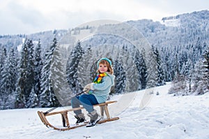 Boy enjoy a sleigh ride. Child sledding, riding a sledge. Children play in snow in winter. Outdoor kids fun for