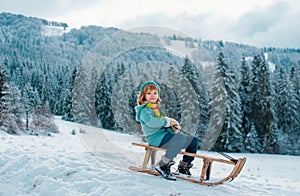 Boy enjoy a sleigh ride. Child sledding, riding a sledge. Children play in snow in winter. Outdoor kids fun for