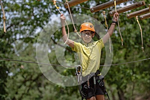 Boy enjoys climbing in the ropes course adventure. Happy boys playing at adventure park holding ropes and climbing wooden stairs