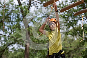 Boy enjoys climbing in the ropes course adventure. Happy boys playing at adventure park holding ropes and climbing wooden stairs