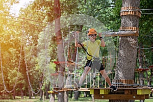 Boy enjoys climbing in the ropes course adventure. Happy boys playing at adventure park holding ropes and climbing wooden stairs