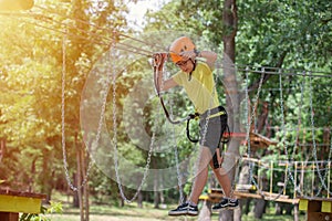 Boy enjoys climbing in the ropes course adventure. Happy boys playing at adventure park holding ropes and climbing wooden stairs