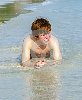 Boy enjoys lying in the spume of the tropical beach
