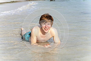 Boy enjoys lying in the spume of the tropical beach