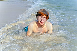 Boy enjoys lying in the spume of the tropical beach