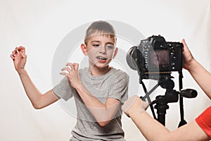 Boy enthusiastically talks to the camera. Children`s hands with a camera in the frame. Young video blogger. White background