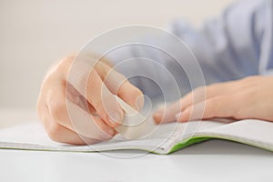 Boy erasing mistake in his notebook at white desk, closeup