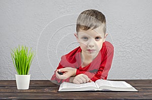 The boy is European. Read book. Open Bible book, on the table. Indoor.