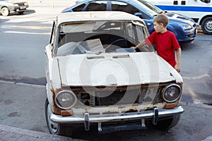 Boy examines rusty with broken windshield car