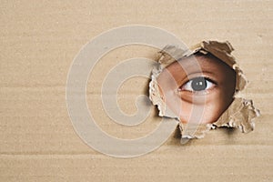 Boy eye peeking through a hole on a cardboard box with shocking gesture.