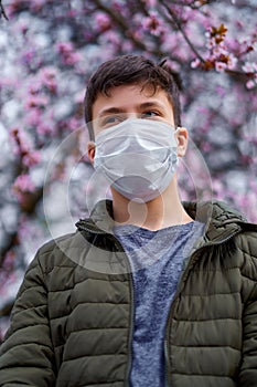 Boy with a face mask is in the city outdoor, blooming trees, spring season, flowering time - concept of allergies and health