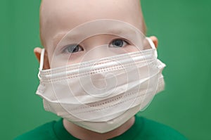 Boy in face mask in a green t-shirt on a green background. child wear facemask during coronavirus and flu outbreak. Virus and photo