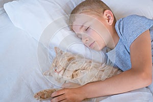 the boy falls asleep and hugs his ginger cat, who sleeps with him under the covers. children and pets. the cat sleeps