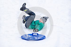 Boy falls rolling down a hill on snow saucer. Winter games