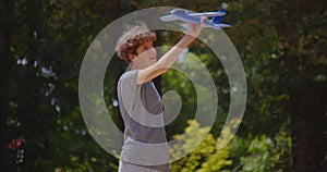 A boy with a fashionable hairstyle plays in the park with a toy airplane. Children playing outside. Happy traveler