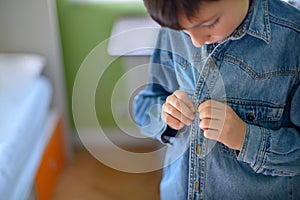 Boy fastens the button of a denim shirt