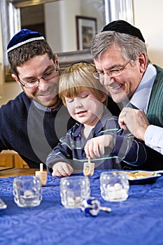 Boy with father and grandfather spinning dreidel