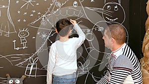 Boy with father paints a picture on the wall with chalk on a Christmas theme