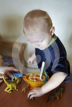 A boy feeds a toy dinosaur porridge from a spoon