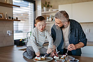Boy filling pancake with fruit, sweets. Father spending time with son at home, making snack together, cooking. Fathers
