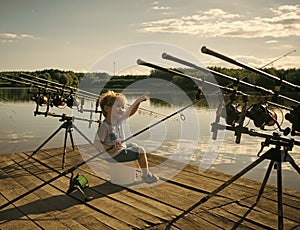 Boy fisherman point finger with fishing rods on wooden pier