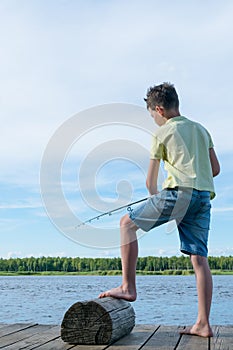 Boy fishes standing on the pier at the lake in the evening