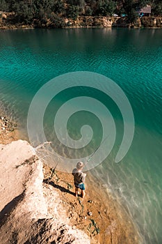 Boy fishing from dock on lake. Kid fishing in clean blue lake in wild nature.