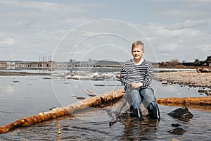 A boy with a fishing rod catches fish sitting on the river bank