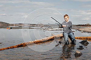 A boy with a fishing rod catches fish sitting on the river bank
