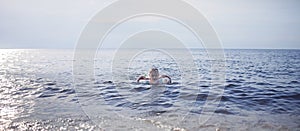 Boy with flotation ring swimming at sea in sunset light, lots of splashes and happiness