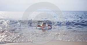 Boy with flotation ring swimming at sea in sunset light, lots of splashes and happiness