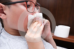 A boy with flu and fever lying in bed and blowing his nose with a paper tissue, seasonal viral diseases concept