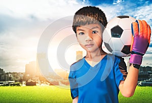 Boy is a football goalkeeper wearing gloves and holding a soccer ball with city background copyspace