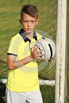 Boy football player in a yellow t-shirt stands near the goal with the ball